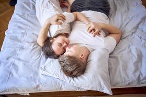 a young couple is lying on the bed, the girl is on the boy's shoulder, tender hugs photo