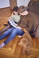 young couple looking at their wedding photo album by the bed in living room, cockapoo running around