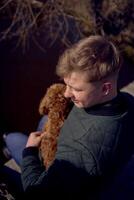 a boy sits on a pier and hugs a cockapoo photo