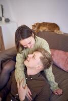 a young couple is hugging on the sofa in the living room, a red cat is sleeping on the back of the sofa photo