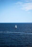 a lone white sailboat surrounded by deep blue water and a clear blue sky photo