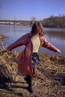 a stylish young woman in a pink trench dances on the bank of a spring river photo