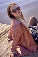 a girl in sunglasses sits on a pier and smiles at the camera photo