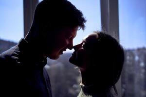 hermosa joven Pareja besos en el iluminar desde el fondo en contra el ventana foto