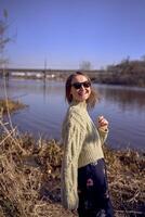 stylish young woman in a light green sweater and sunglasses on the bank of a spring river photo