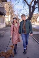 un joven Pareja en amor caminando mediante el primavera ciudad con un cockapoo foto