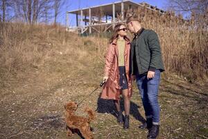 a young stylish couple walking with their cockapoo dog near the river, an unfinished parking lot in the background photo