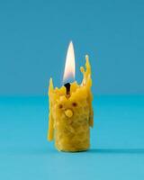 Creative composition made with burnt out yellow beeswax candle melting and creating silly funny face on blue background. Minimal timeline concept. Trendy beeswax candle idea. photo