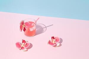 Summer scene made with pink tropical refreshing drink and orchid flowers on pink and blue background. Sun and shadows. Minimal cocktail concept. Trendy summertime party idea. Summer aesthetic. photo