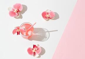 Summer scene made with pink tropical refreshing drink and orchid flowers on white and pink background. Sun and shadows. Minimal cocktail concept. Trendy summertime party idea. Summer aesthetic. photo