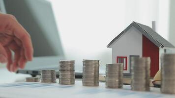 Real estate concept background. House model and coins stack on wooden table, copy space. video