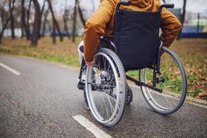 Close up image of paraplegic handicapped man in wheelchair in park. He is rolling on pathway. photo