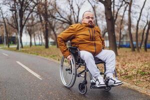 Portrait of paraplegic handicapped man in wheelchair in park. He is rolling on pathway. photo