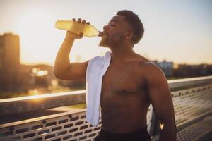 Portrait of young african-american man who is drinking water and relaxing after jogging. photo
