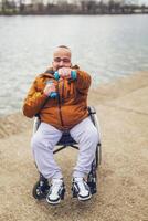 contento parapléjico minusválido hombre en silla de ruedas por el lago. él es Listo para ejercicio con pesos foto