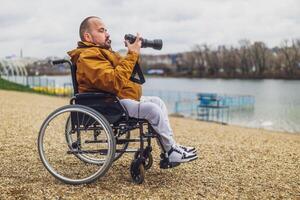 parapléjico minusválido hombre en silla de ruedas es fotografiando exterior. foto