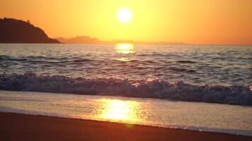 gyllene solnedgång på de strand. skummig vågor rullande mot gyllene sand strand under låg värma Sol ljus. långsam rörelse. ingen. Semester rekreation begrepp. abstrakt nautisk sommar hav solnedgång natur. video
