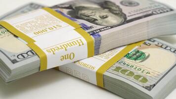 stack of bank bundles with US dollars on a white background. Close-up shot of new, freshly printed hundred-dollar bills rotating on a table. cash flow, business investment, or big money concepts. video