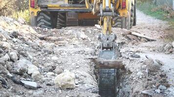 Excavator digs a trench to lay pipes. Close up of an excavator digging a deep trench. An excavator digs a trench in the countryside to lay a water pipe. Slow motion video