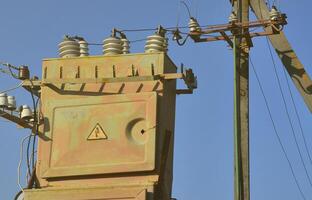 Old and obsolete electrical transformer against the background of a cloudless blue sky. Device for distribution of supply of high-voltage energy photo