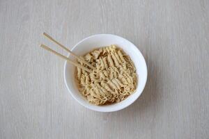 Bowl of instant cooking noodles with wooden chopsticks on white wooden table photo