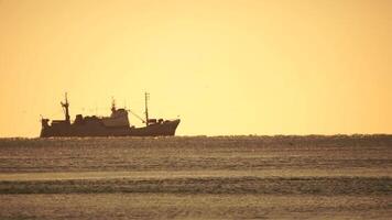 silhouet van visvangst schip in de zee Aan horizon. schip het zeilen in de zee. klein golven Aan de gouden oppervlakte van warm water met bokeh lichten van de zon. zee, natuur en buitenshuis reizen. video