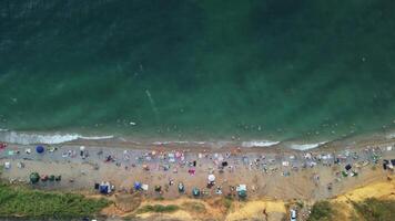 Aerial timelapse of sandy beach, swimming people in sea bay with transparent blue water at sunset in summer. People Crowd Relaxing On Beach. Holiday recreation concept. Abstract summer ocean sunset video