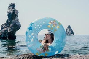 mujer verano mar. contento mujer nadando con inflable rosquilla en el playa en verano soleado día, rodeado por volcánico montañas. verano vacaciones concepto. foto