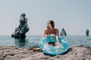 mujer verano mar. contento mujer nadando con inflable rosquilla en el playa en verano soleado día, rodeado por volcánico montañas. verano vacaciones concepto. foto