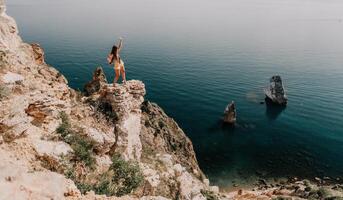 Woman travel sea. Happy tourist enjoy taking picture outdoors for memories. Woman traveler looks at the edge of the cliff on the sea bay of mountains, sharing travel adventure journey photo