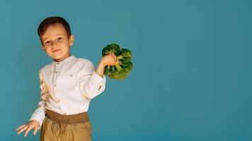 A studio shot of a boy holding fresh broccoli on a blue background with a copy of the space. The concept of healthy baby food. photo