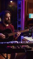 Vertical Video Music producer tuning his acoustic guitar before playing instrument, recording and mixing tunes to create new soundtracks. Singer composing a song using electronic panel controls. Camera B.