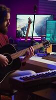 Vertikale Video Musiker versuchen zu Melodie das Klang von seine Gitarre im Zuhause Studio, einstellen Knöpfe Vor spielen Melodien und Aufzeichnung auf Morgengrauen Software. fortgeschritten Mischen und meistern Techniken. Kamera b.