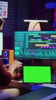 verticaal video musicus menging en beheersen geluiden Bij huis studio met elektronisch troosten en klankbord, creëren modern melodieën. geluid ingenieur produceren audio sporen met groene scherm Aan tablet. camera b.