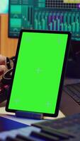 vertical vídeo música productor compositor de canciones mezcla melodías en estéreo consola, grabación sonidos siguiente a tableta con pantalla verde disposición. artista utilizando igualada y controlar panel junta, grajilla software. cámara una. video