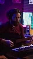 Vertical Video Musical composer recording his guitar tunes and adding piano key sounds, creating a beautiful song with mixing console and daw software. Sound engineer working with electronic tools. Camera B.