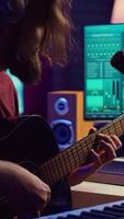 Vertical Video Artist composing a song with his acoustic guitar in home studio, recording notes and singing melody on microphone. Sound engineer mixing and mastering his tunes with stereo equipment. Camera A.