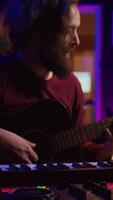 Vertical Video Artist composing a song with his acoustic guitar in home studio, recording notes and singing melody on microphone. Sound engineer mixing and mastering his tunes with stereo equipment. Camera B.