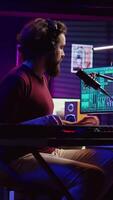 verticaal video geluid ingenieur drukken sleutels van elektrisch synthesizer en opname nieuw muziek, aanpassen lawaai niveau. artiest het zingen lied Aan microfoon, werken met menging bord in huis studio. camera b.