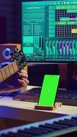 verticale video giovane musicista Guardando lezione lezione per sintonizzare il suo chitarra stringhe, sembra a schermo verde disposizione su Telefono. artista apprendimento per giocare acustico strumento, praticante su in linea musicale classe. telecamera un.