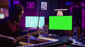 Male singer learning to play a new song on acoustic guitar, using greenscreen on computer to watch online video tutorials. Artist songwriter practicing with his instrument in home studio. Camera B.