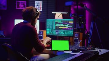 Musician mixing and mastering sounds at home studio with electronic console and soundboard, creating modern tunes. Sound engineer producing audio tracks with greenscreen on tablet. Camera B. video