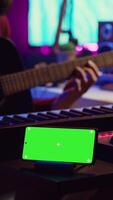 vertical vídeo compositor de canciones jugando acústico guitarra en hogar estudio con pantalla verde monitor corriendo en teléfono inteligente aplicación músico practicas canto en musical instrumento con instrumentos de cuerda, aislado pantalla. cámara una. video