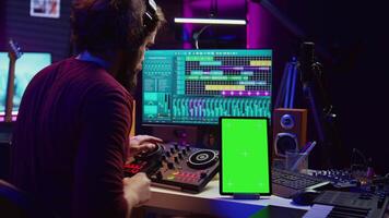 música productor compositor de canciones mezcla melodías en estéreo consola, grabación sonidos siguiente a tableta con pantalla verde disposición. artista utilizando igualada y controlar panel junta, grajilla software. cámara b. video