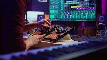 Artist editing sounds on mixing console in home studio, operating professional audio equipment to adjust volume levels on track recordings. Musician works with daw software an pre amp knobs, Camera B. video