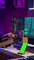 vertical vídeo artista aprendizaje a melodía su acústico guitarra con aplicación tutorial, utilizando pantalla verde monitor en teléfono inteligente un practicando música lecciones joven músico haciendo ensayo con instrumento. cámara b. video