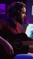 Vertical Video Sound engineer playing acoustic guitar and using mixing console to record music, adjusting volume and adding sound effects to tunes. Artist works with digital audio workstation software. Camera B.