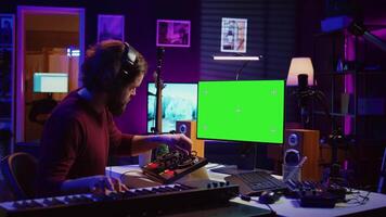 Audio engineer learning to mix piano notes with mixing console, watches online lesson tutorials on greenscreen monitor display. Music producer creating soundtracks, learns editing skills. Camera B. video