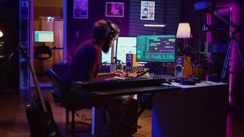 blij artiest spelen piano toetsenbord en opname deuntjes voor menging en beheersen sessie, genieten van midi controleur prestatie in huis studio. energiek muziek- producent creëren soundtracks. camera b. video