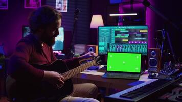 musicus aan het leren naar Speel nieuw akoestisch instrument in zijn huis studio, beoefenen online gitaar lessen Aan geïsoleerd groene scherm Scherm. aan het kijken zelfstudie Aan laptop naar ontwikkelen zijn vaardigheden. camera b. video